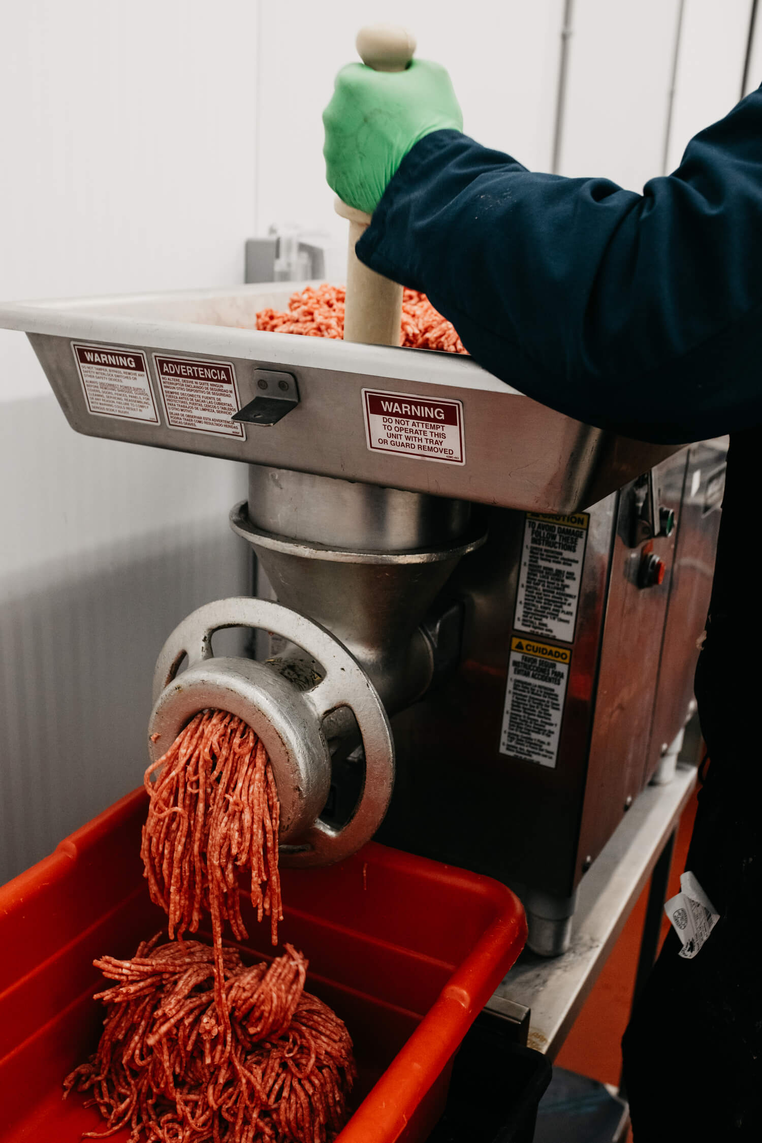 Ground meat being processed through a grinder into a red container.