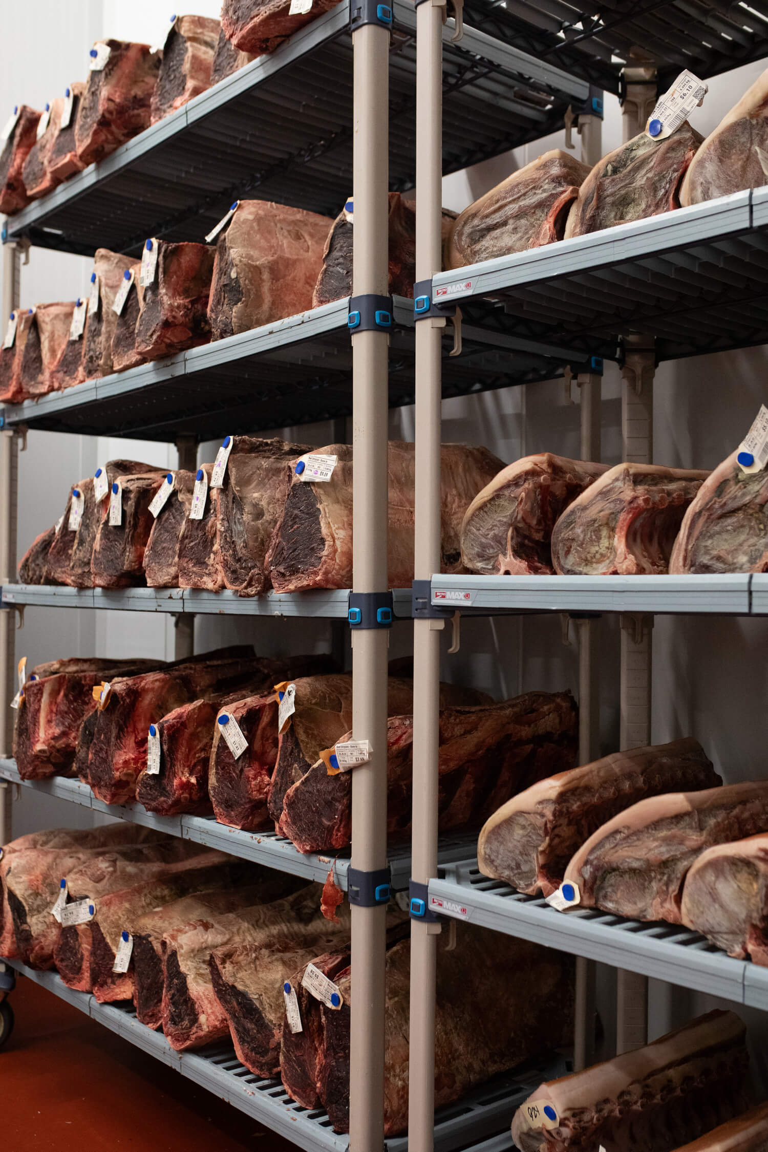 Large cuts of meat arranged on metal shelving in a storage room.