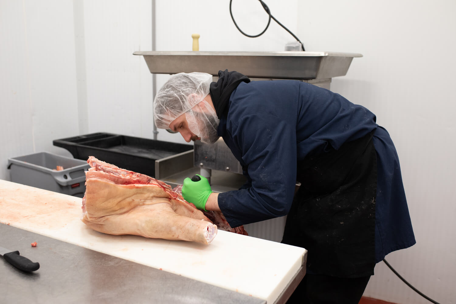 Butcher cutting a large piece of meat on a work surface.