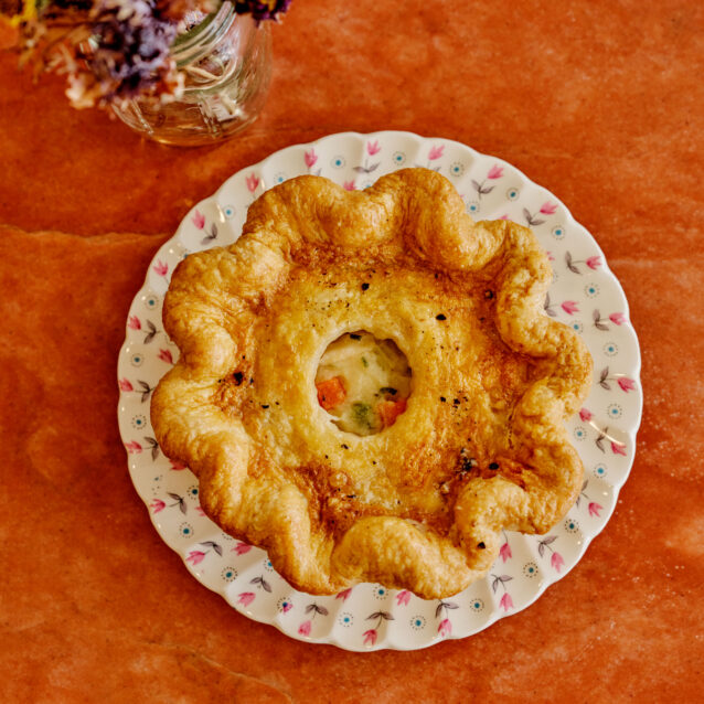 Individual apple crumble pie on a decorative plate with flowers on an orange surface.